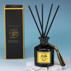 Diffusore di profumo per ambiente in bottiglia nera con bastoncini diffusori e nappina decorativa, accompagnato da scatola coordinata con dettagli dorati su sfondo azzurro.