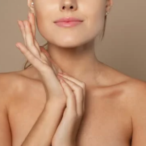 Primo piano di una donna con pelle liscia che tocca delicatamente il viso con le mani, su sfondo neutro, concetto di skincare e bellezza naturale.