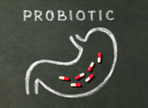 Lavagna con disegno stilizzato dello stomaco e la scritta “probiotici”, con capsule rosse e bianche all’interno, concetto di integratori per la salute digestiva.