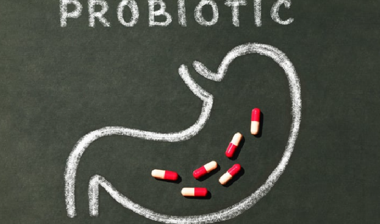 Lavagna con disegno stilizzato dello stomaco e la scritta “probiotici”, con capsule rosse e bianche all’interno, concetto di integratori per la salute digestiva.