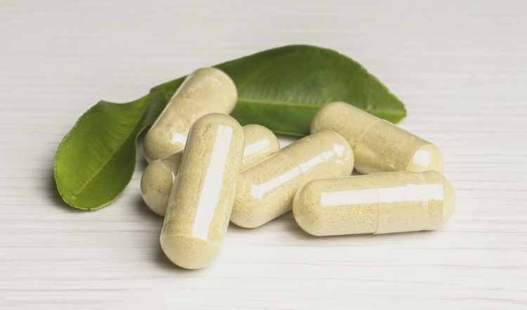 Capsule di berberina naturale contenenti estratti vegetali, adagiate su una superficie bianca con foglie verdi sullo sfondo, simbolo di benessere e nutraceutica.