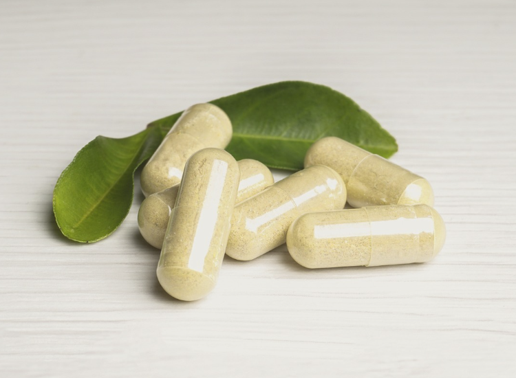 Capsule di berberina naturale contenenti estratti vegetali, adagiate su una superficie bianca con foglie verdi sullo sfondo, simbolo di benessere e nutraceutica.